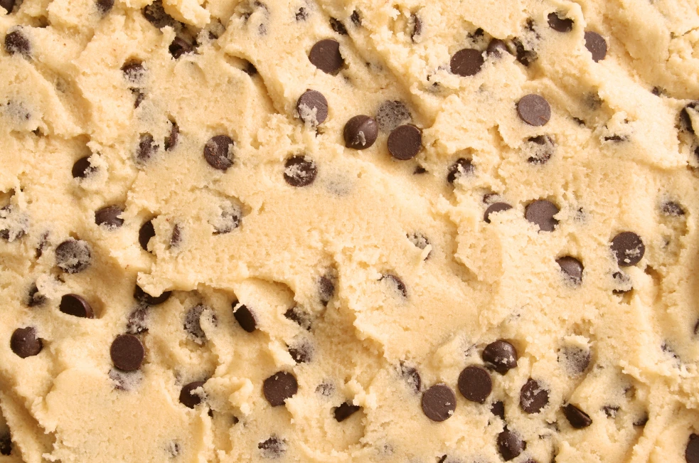 Raw Nestlé cookie dough alongside freshly baked cookies on a rustic wooden table.