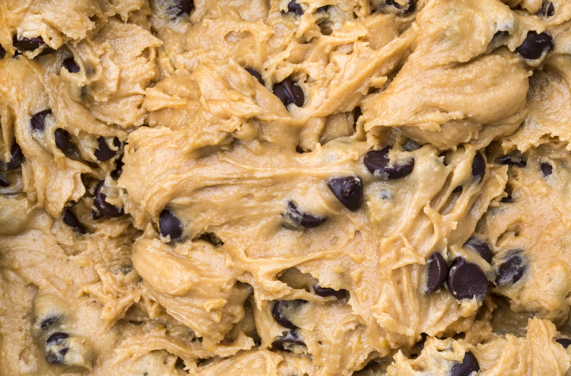 Raw Nestlé cookie dough alongside freshly baked cookies on a rustic wooden table.