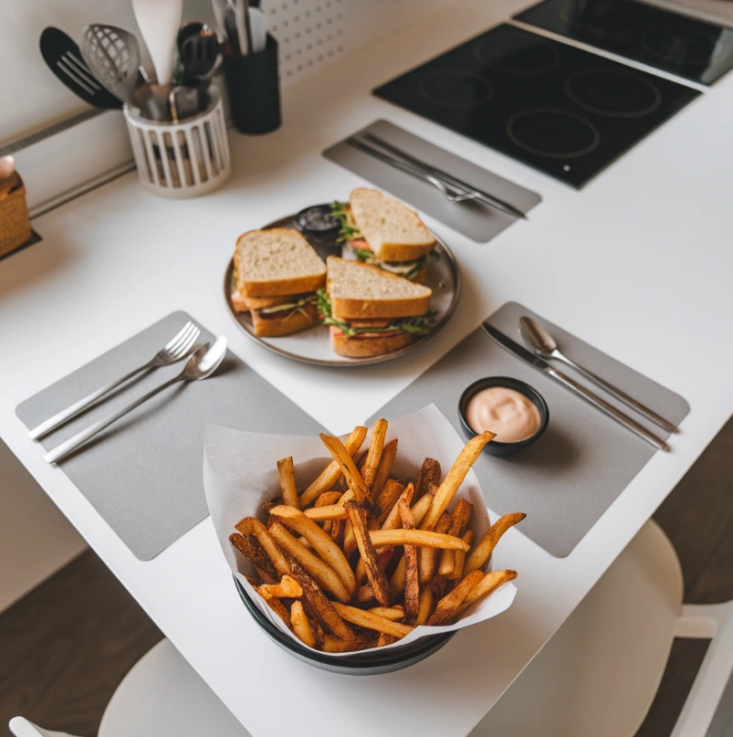 A plate of sandwiches paired with crispy hot fries and a small bowl of dipping sauce on a modern kitchen table.