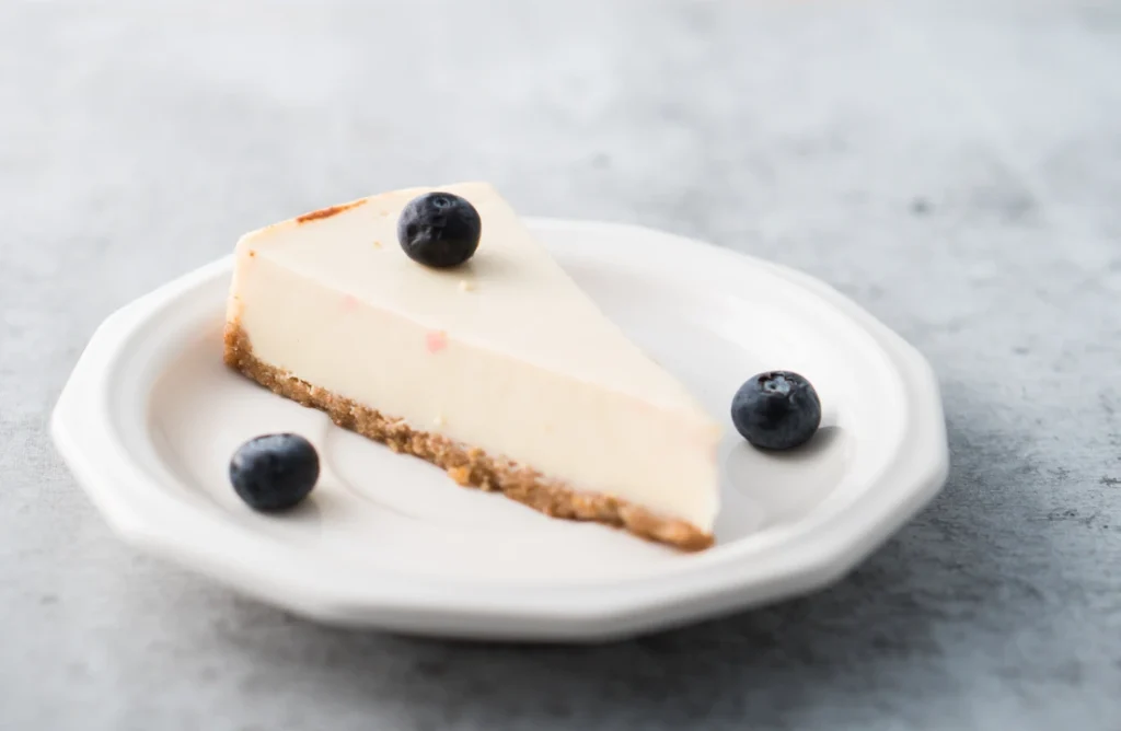 A creamy, classic cheesecake with a golden crust and fresh berry topping on a white plate.