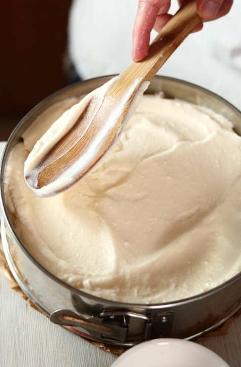 A mixing bowl with cheesecake batter ingredients like cream cheese, sugar, eggs, and vanilla.