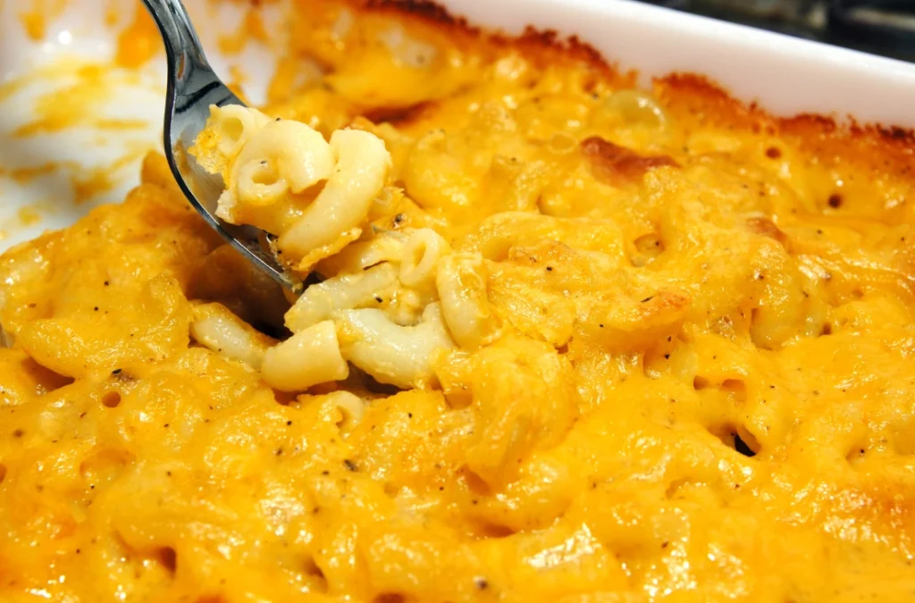 A steaming bowl of macaroni and cheese garnished with bacon, herbs, and breadcrumbs.