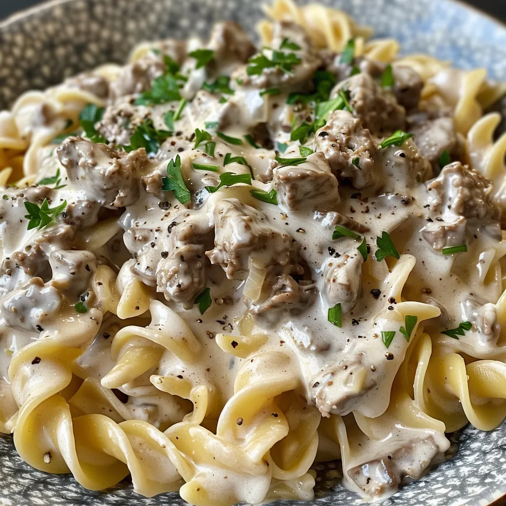 Close-up of a skillet of garlic parmesan beef stroganoff with egg noodles and a creamy sauce.